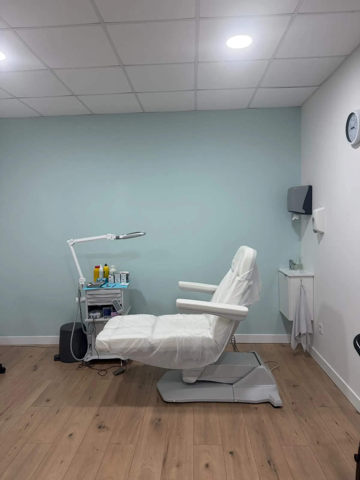 Consulta de podología con sillón, carro de instrumental, lavabo y reloj de pared. Clínica Paula Vega, Leganés