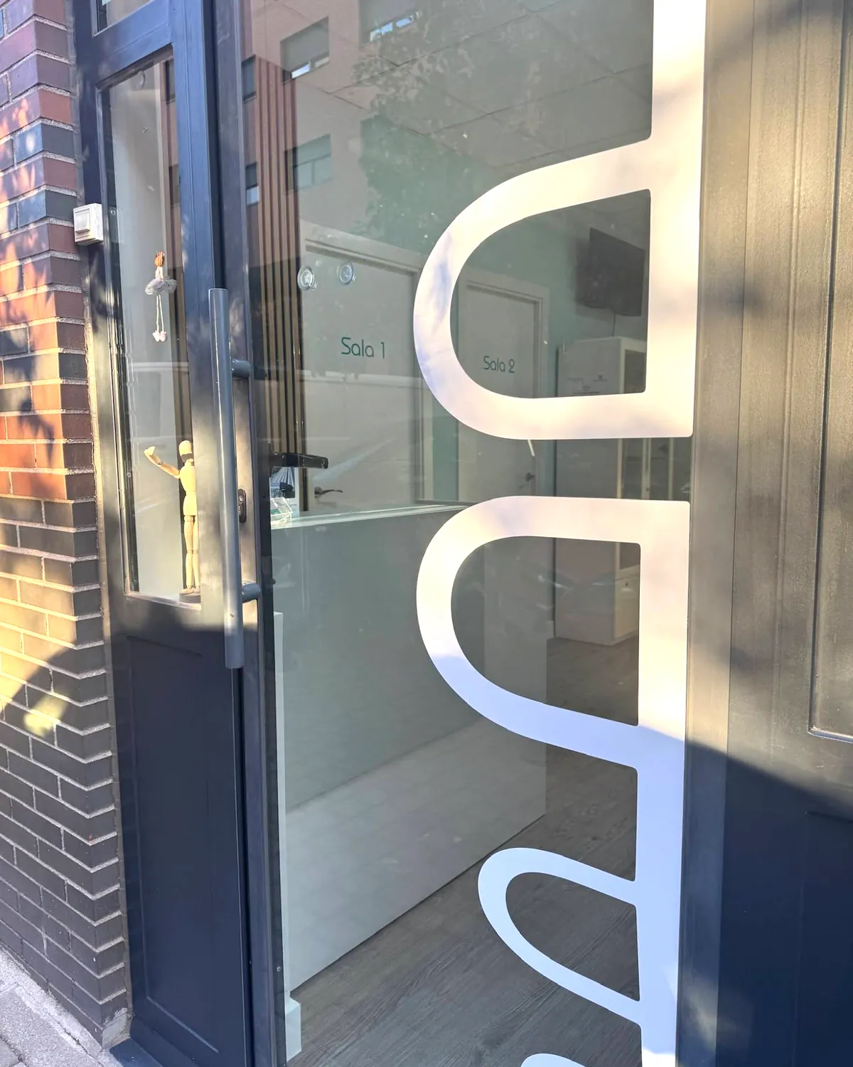 Puerta de entrada de la clínica entreabierta, con el logo en el cristal y las salas 1 y 2 al fondo