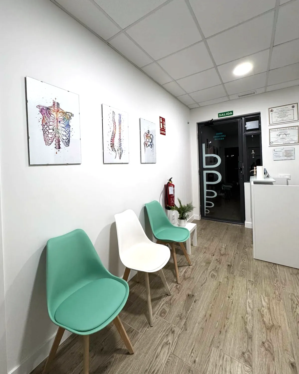 Recepción y puerta de entrada de la Clínica Paula Vega, con los diplomas de osteopatía en la pared