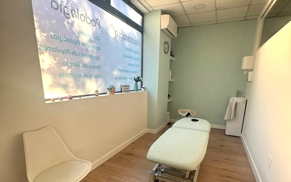 Sala de podología y fisioterapia con camilla y la ventana rotulada con los servicios de la clínica