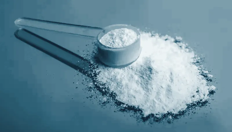Cuchara medidora con suplemento en polvo blanco sobre fondo azul