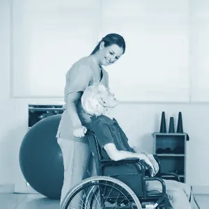 Fisioterapeuta ayudando a una mujer mayor en silla de ruedas en una sala de rehabilitación
