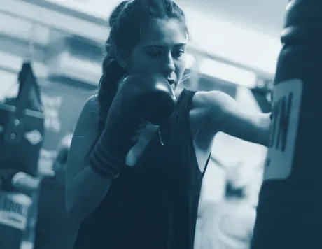 Mujer con guantes de boxeo golpeando un saco en el gimnasio