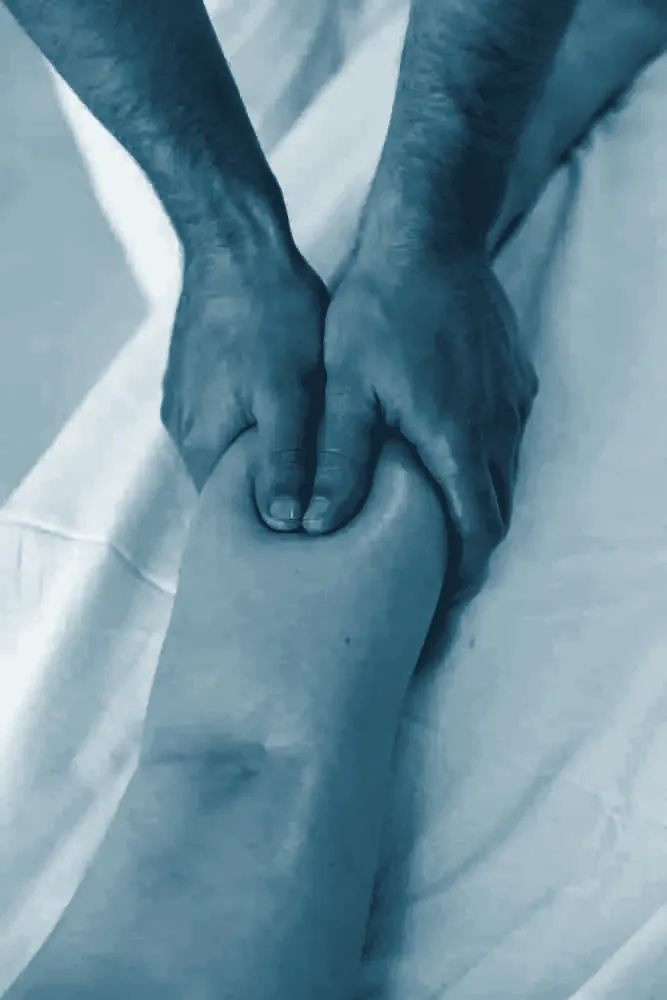 Manos de fisioterapeuta masajeando el muslo por encima de la rodilla