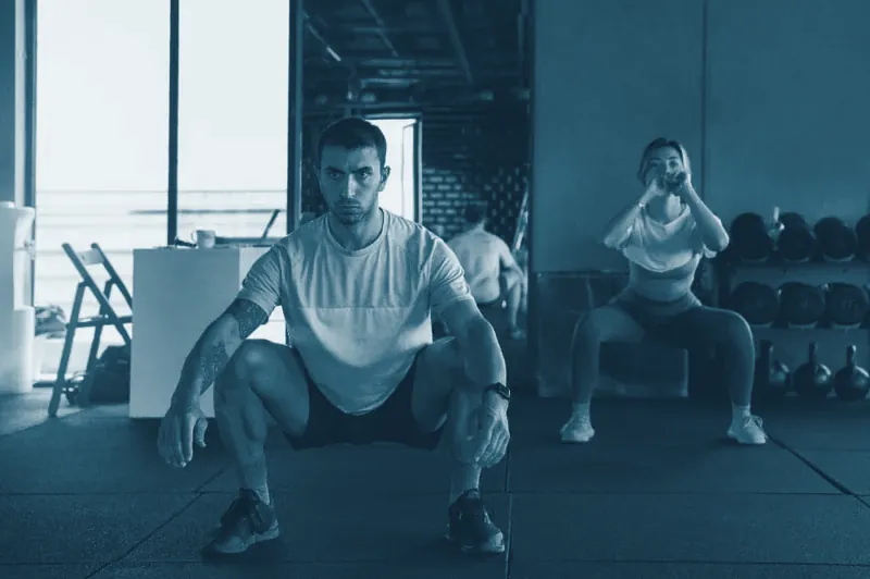Dos personas haciendo sentadillas en un gimnasio