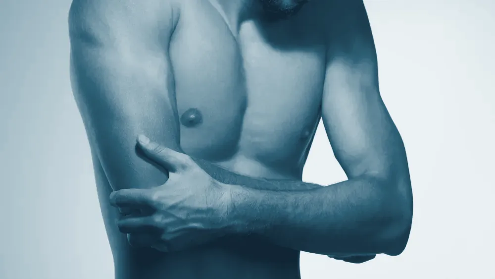 Hombre sujetándose el brazo con la zona de dolor del hombro y el codo marcada en rojo